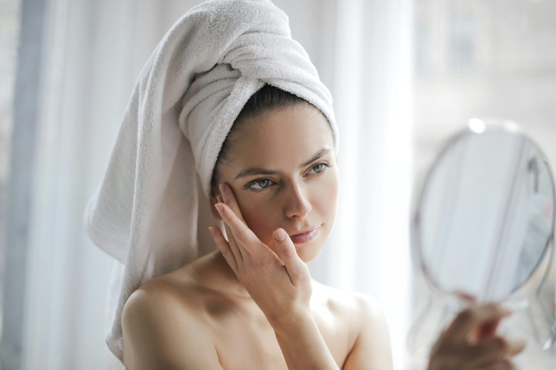 Woman with a towel checking her skin in a mirror